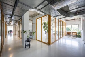 Moderne kantoorruimte aan de Anthony Fokkerweg met glazen vergaderruimtes, planten en industrieel plafond.